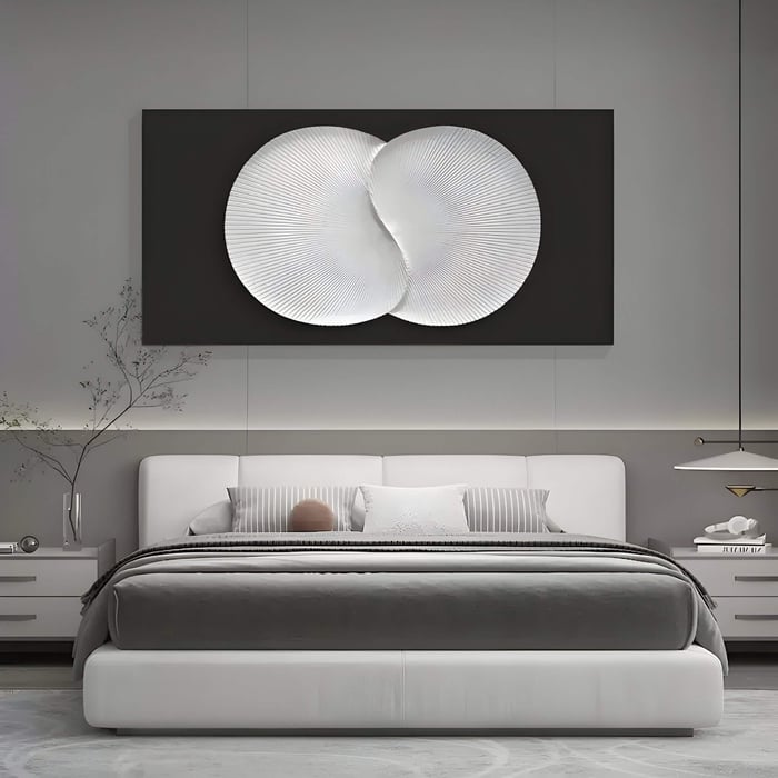 A modern bedroom features a large white bed with striped pillows and a gray blanket, adorned by the Artivio Black & White Wood Relief 3D Wall Art from Giant Sculptures above it. Minimalist decor includes small plants on the nightstands and a sleek pendant light.