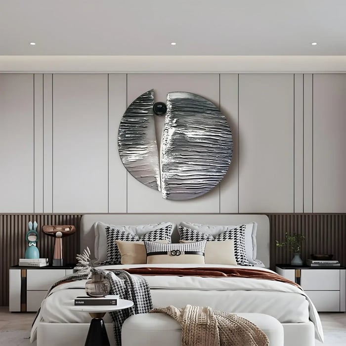  A contemporary bedroom with a statement silver wall sculpture, featuring a split circular design with textured surfaces, mounted above a bed with houndstooth and neutral bedding.