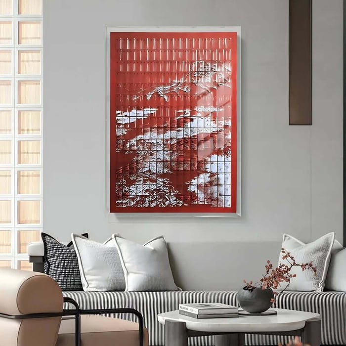 Red framed textured wall art with raised details above a modern sofa in a minimalist living room.