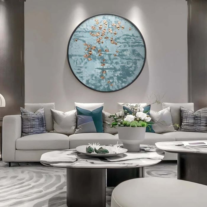 Round blue wall artwork with gold leaf accents above a light sofa in a calm, minimalist lounge.