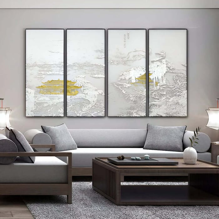 Four-panel wall art set with white relief landscape details and gold accents above a grey sofa.