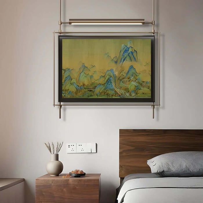 Framed mountain landscape painting above a bed with wooden headboard in a minimalist bedroom.