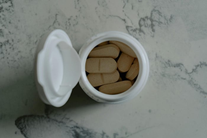 Opened bottle of beige pills on marbled surface