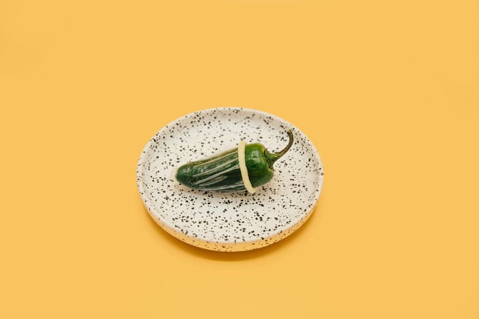 An aesthetic yellow photo of a green chili on a plate with a condom on it