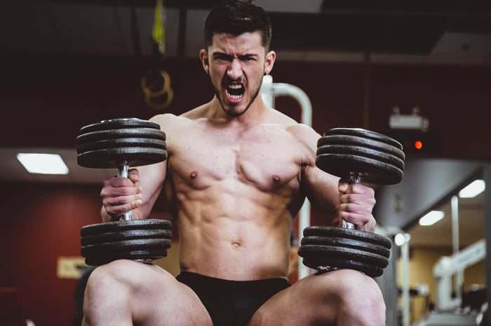 A man roaring into the camera while lifting weights at the gym