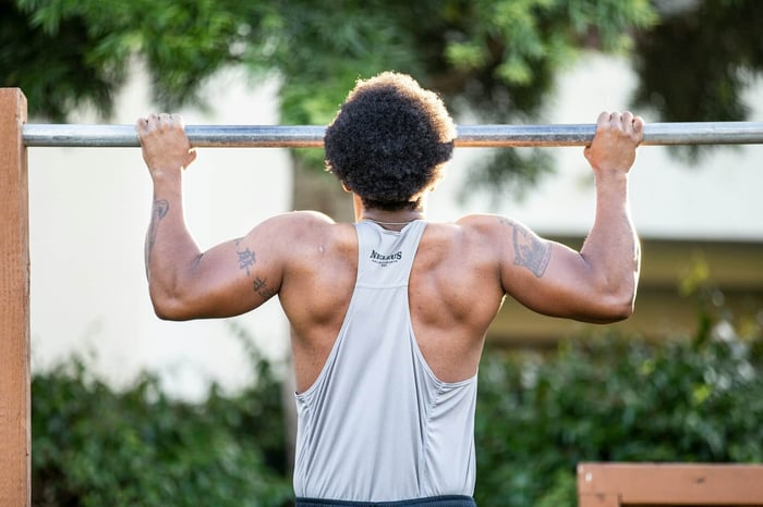A muscular guy holds himself up on a steel bar with a firm grip on both ends