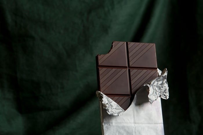A bar of dark chocolate unwrapped with a bite missing from the top corner