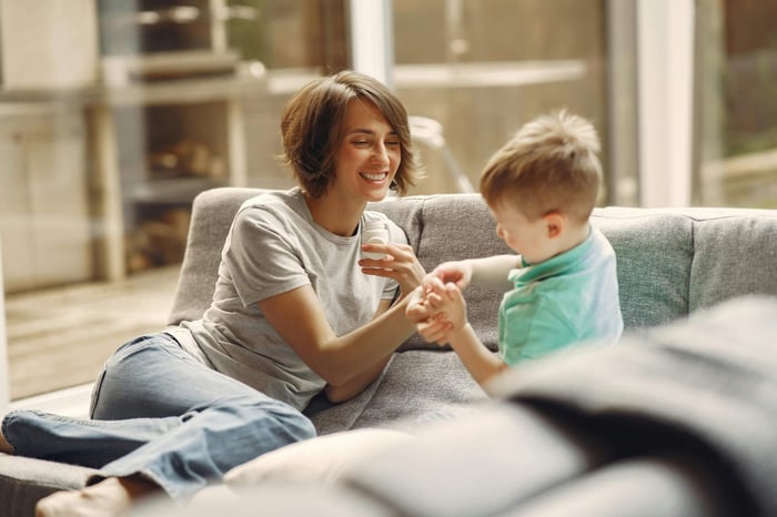 A woman smiles while she plays with her son on a couch in a well lit interior space.