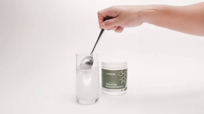 An arm comes out from the top right corner of the image holding a spoon while stirring a MyFitFoods Creatine product.