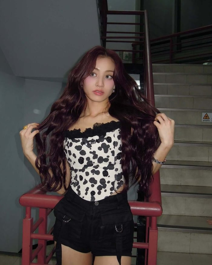 TWICE's Jihyo is proving that the all-over raspberry hair trend is a stunning and low-maintenance alternative to highlights, demonstrating how this rich, single-shade color can create a dimensional and captivating look when paired with bouncy curls.