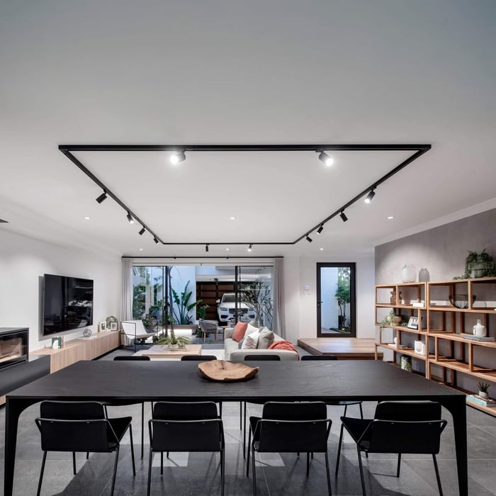 Modern open-plan living and dining space featuring black track lighting on the ceiling, neutral furniture, and open shelving.