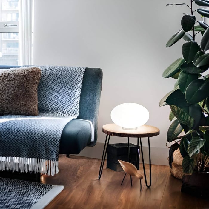 Scandinavian-style lounge with a round wooden side table, glowing white orb lamp, and a blue sofa near leafy indoor plant.