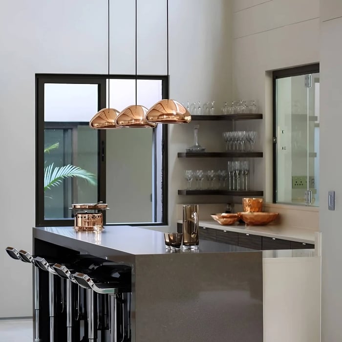 Modern kitchen island with four copper dome pendant lights over a sleek grey countertop.