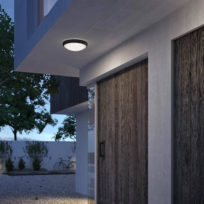 Round flush outdoor ceiling light mounted above a front entrance with large timber doors.