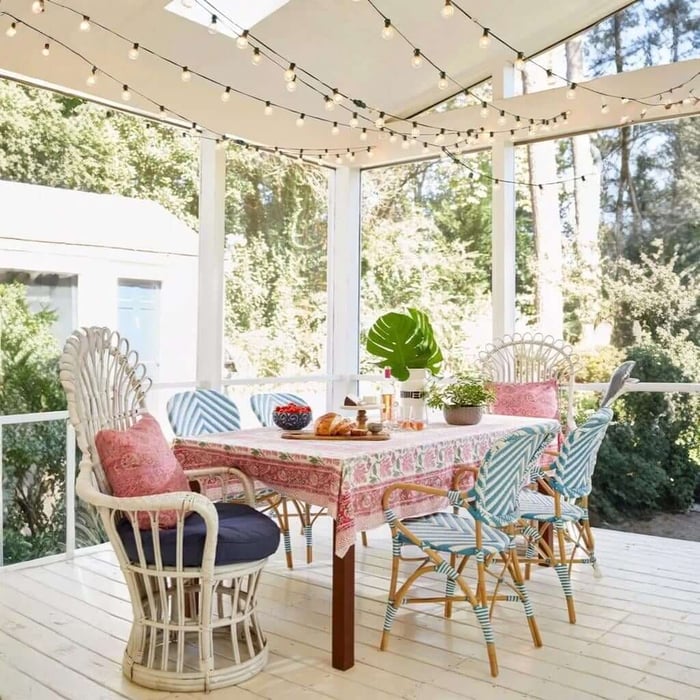 Outdoor string lights zig-zagged across a covered porch above a dining table with colourful chairs in daylight.