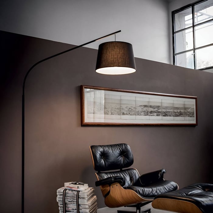 Contemporary arc floor lamp with black shade illuminating a leather lounge chair.