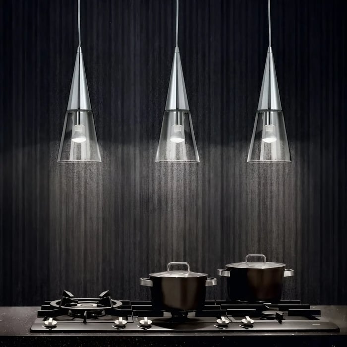 Set of three cone-shaped glass pendant lights hanging over a dark kitchen counter with a stove and pots beneath.