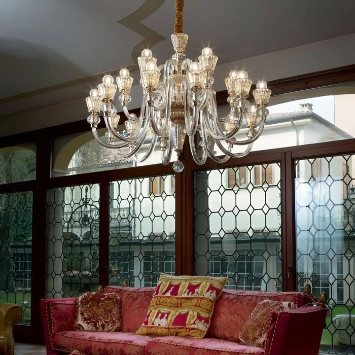 A luxurious room with a large glass chandelier with multiple branches, suspended over a red patterned sofa in an elegant room with decorative windows. From the Glass Chandeliers collection 