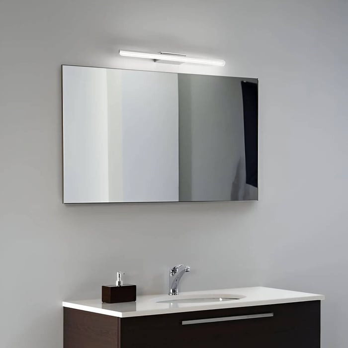 Slim LED bathroom mirror light mounted above a wide rectangular mirror and modern vanity.