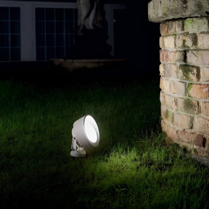 White ground spotlight illuminating a brick wall on a lawn at night.