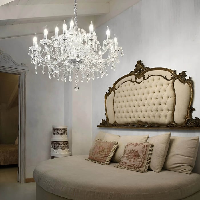 Large crystal chandelier above a bed with a carved vintage headboard in a soft-toned bedroom.
