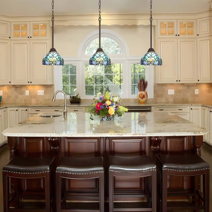 Trio of blue and green Tiffany pendant lights above a kitchen island with dark wood cabinetry and a cream-toned traditional interior.