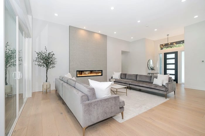  Open-concept living room with a sleek, minimalist aesthetic, featuring gray sectional sofas, a modern fireplace, and bright recessed downlights, creating a spacious and airy feel.