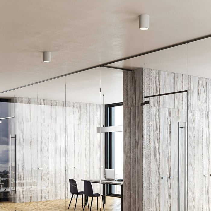 Contemporary office with white cylindrical downlights installed across ceiling and wood-panelled walls.
