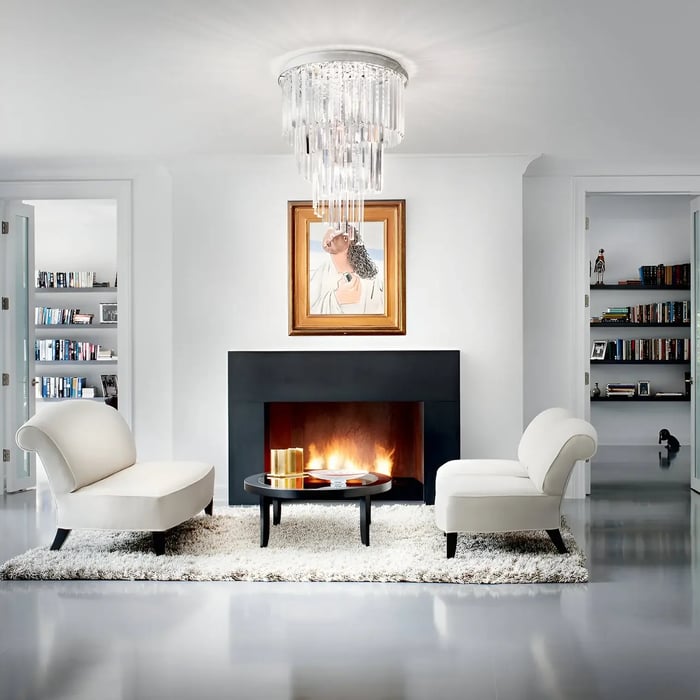 Cozy modern living room with glass chandelier, white lounge chairs, and black fireplace with a portrait and soft rug.