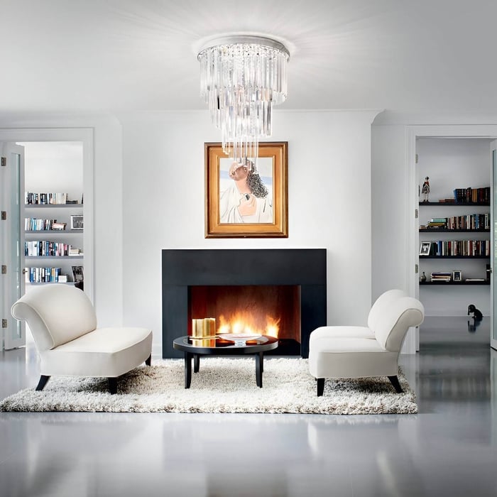 Tiered crystal flush mount chandelier in a minimal fireplace lounge with two sculptural armchairs.