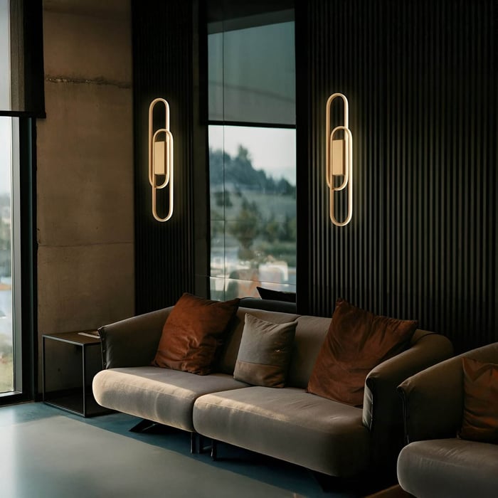 Modern lounge with dark paneled walls, plush gray sofa, brown accent pillows, and geometric glowing wall sconces.