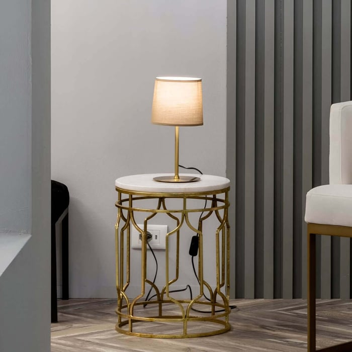 Elegant gold and white table lamp on a round marble-top side table in a stylish, modern interior.