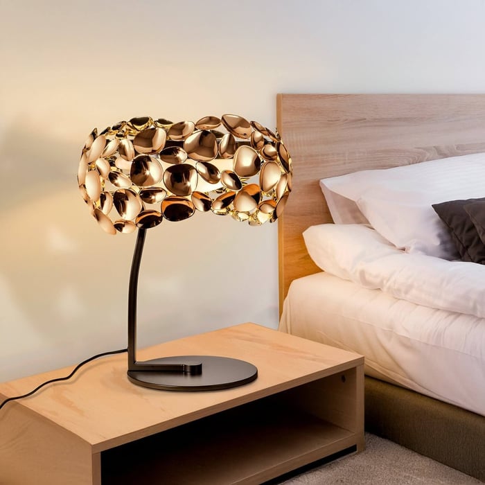 Artistic gold table lamp with sculpted shade on a wooden bedside table in a cozy bedroom.