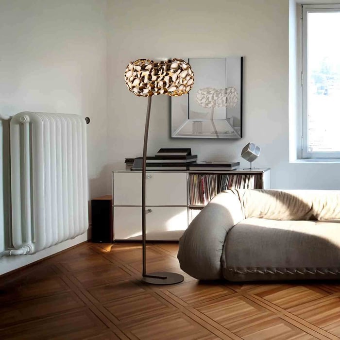 Sculptural floor lamp with leaf-pattern shade beside grey sofa and white sideboard in a sunlit living room.
