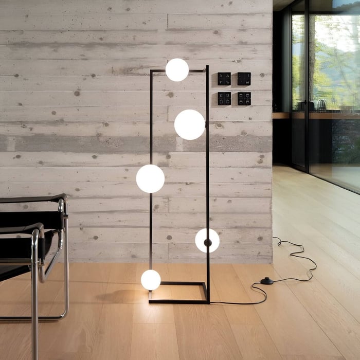 Black frame floor lamp with five glowing opal globes arranged vertically in a contemporary interior with concrete walls.
