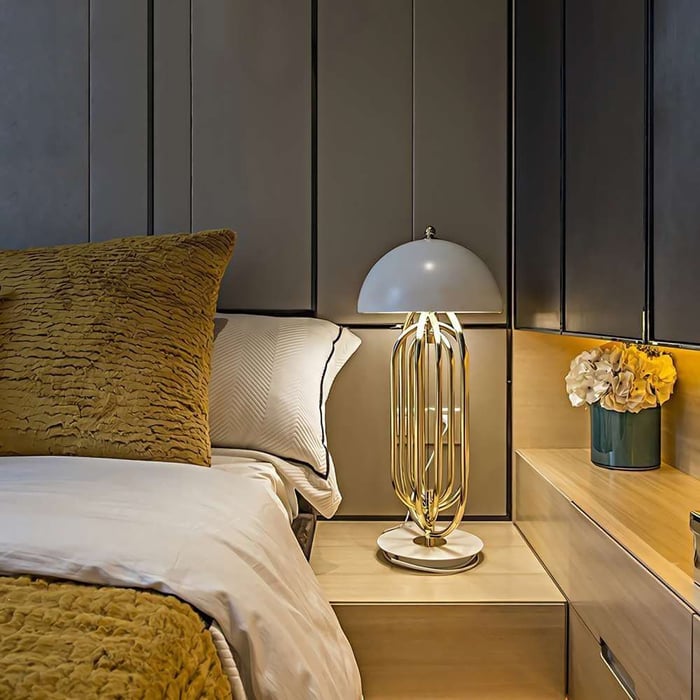 Contemporary bedroom with gold table lamp, plush bedding, and nightstand decor including a flower vase.