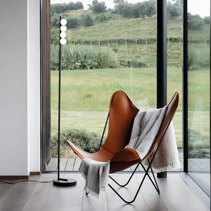 Slim modern floor lamp with vertical row of glowing orbs beside a leather lounge chair.