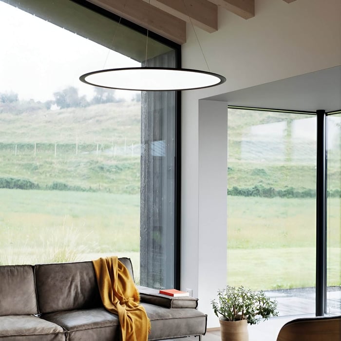 Large circular pendant light hanging in a bright modern living room with floor-to-ceiling windows and a leather sofa.
