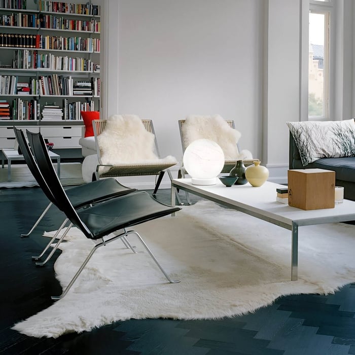 Minimal living room with a white coffee table, globe lamp, and cozy seating with fur throws, backed by a large bookshelf.
