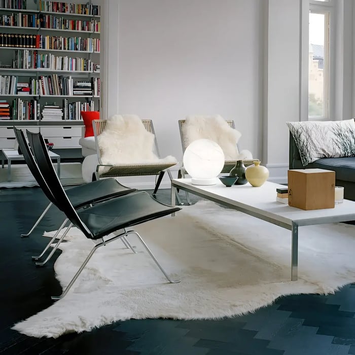 A sleek living space with black leather chairs, a white coffee table adorned with ceramic vases and a glowing globe lamp, surrounded by a built-in bookshelf and accented with a soft white rug on dark flooring.