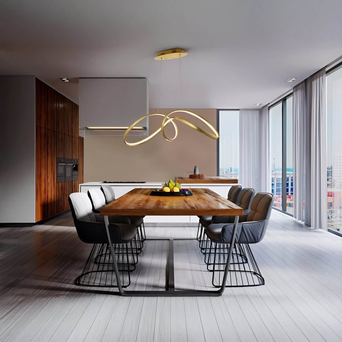 Gold sculptural chandelier with ribbon-like design hanging above a wooden dining table with eight chairs.