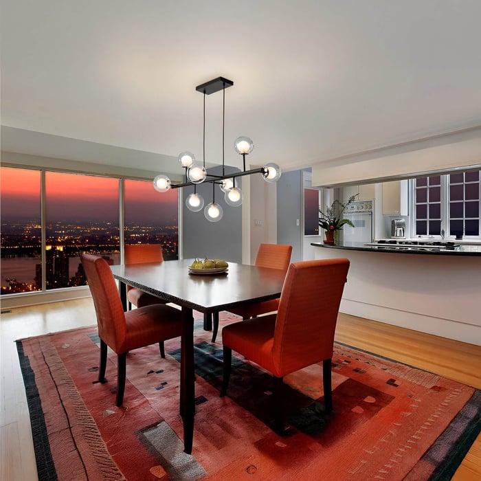 Dining room at sunset with cluster globe pendant light above a dark wood table and red upholstered chairs.