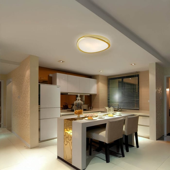 Modern kitchen with ceiling-mounted gold-accented flush light, cream cabinetry, and small breakfast island with beige chairs.