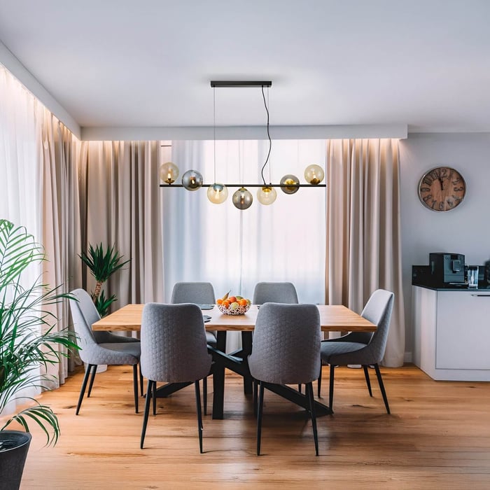 Pendant bar chandelier with mixed glass globe bulbs above a wooden dining table and six grey upholstered chairs.