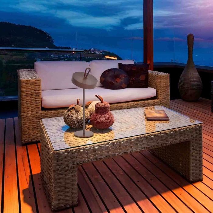 Evening balcony lounge with wicker sofa and coffee table, styled with a portable outdoor table lamp and decorative accessories.
