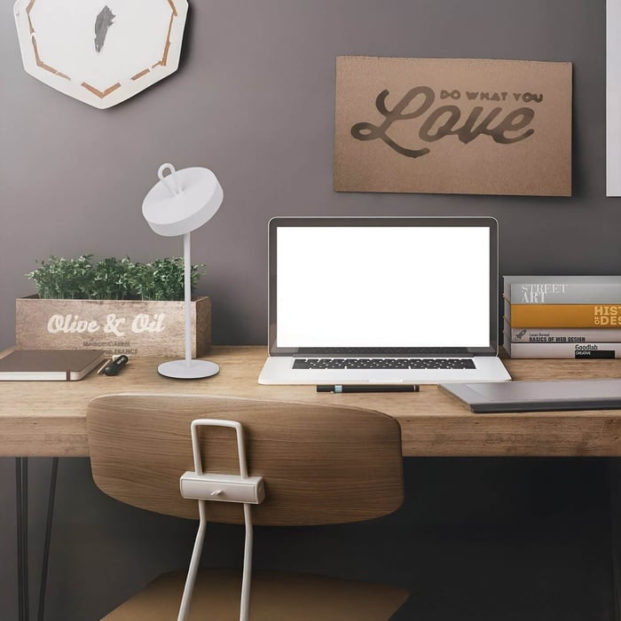 Modern home office setup with a white desk lamp, open laptop, motivational wall art, and books on a wooden desk.