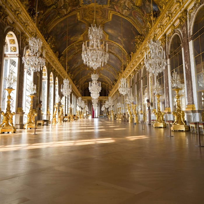 Grand palace hall with gilded décor, mirrored walls, and multiple large crystal chandeliers hanging from a painted ceiling.