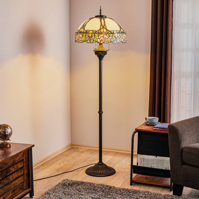 Tall floor lamp with dome-shaped Tiffany glass shade and bronze base in a cozy corner next to an armchair