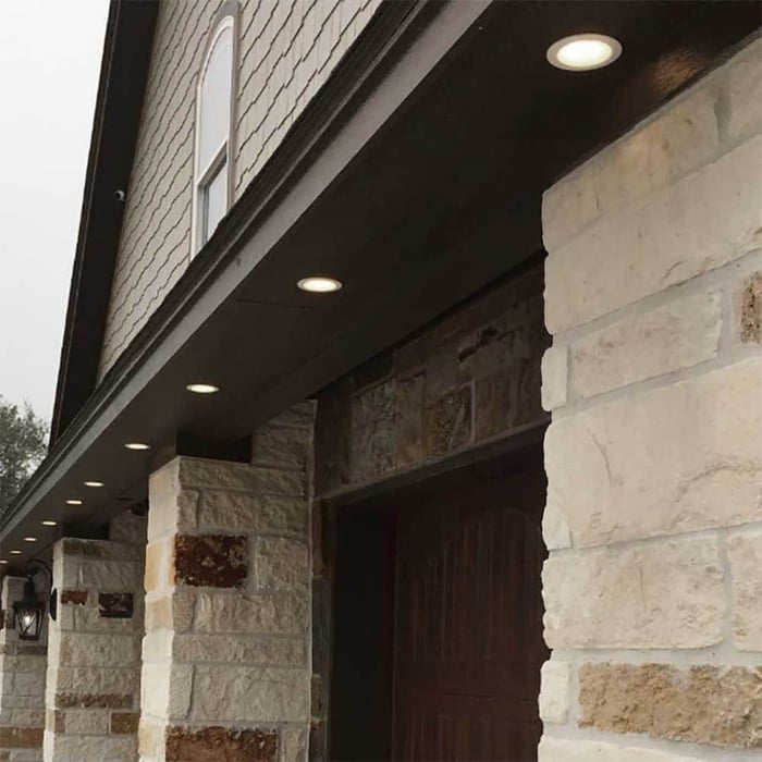 Row of recessed soffit downlights paired with black lantern wall lights on a stone exterior.