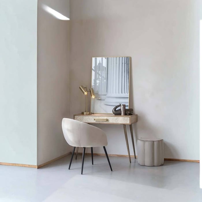 Neutral dressing-table corner with a gold twin-head table lamp beside a mirror and upholstered chair.